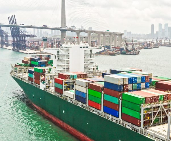 Large cargo ship transporting shipment container arriving Hong Kong port, bridge and city background, drone aerial view. Freight transportation, import export business or industrial concept